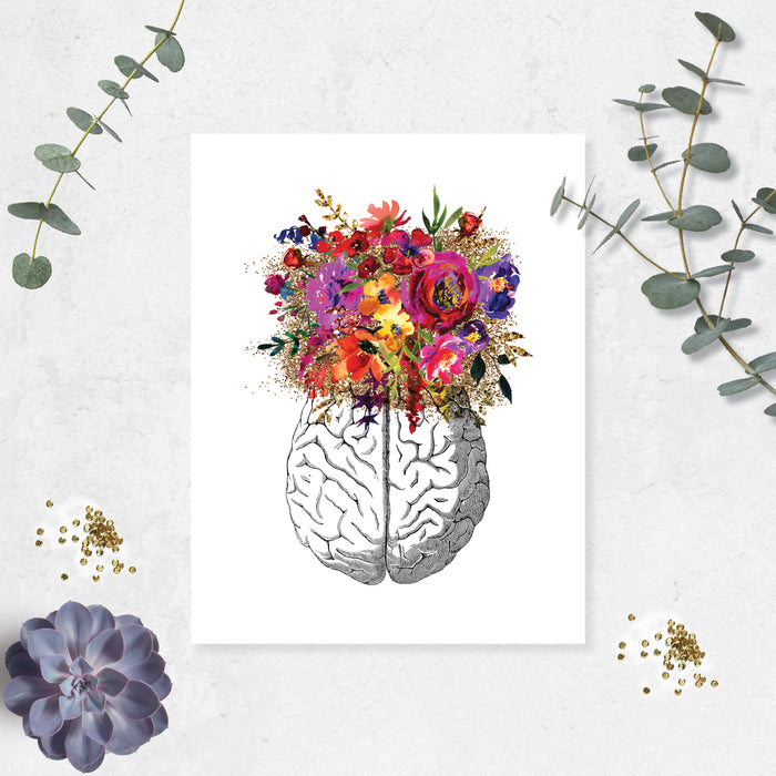 vintage etching of the top view of a brain topped with watercolor flowers in shades of pink, purple, golden and yellow toneson matte white paper