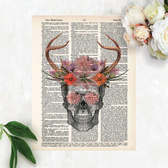 pencil sketch of a skull with watercolor antlers and flowers in pinks, purples, and salmon tones with flowers covering the eyes printed on a dictionary page